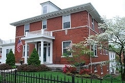 Large two-story brick house with columned porch and black wrought-iron fence