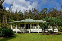 White house with green roof, large porch, green lawn, trees and blue sky
