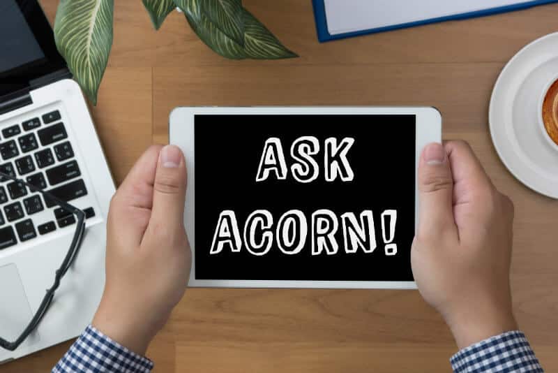 Man's hands holding a tablet that says "Ask Acorn!" at a desk