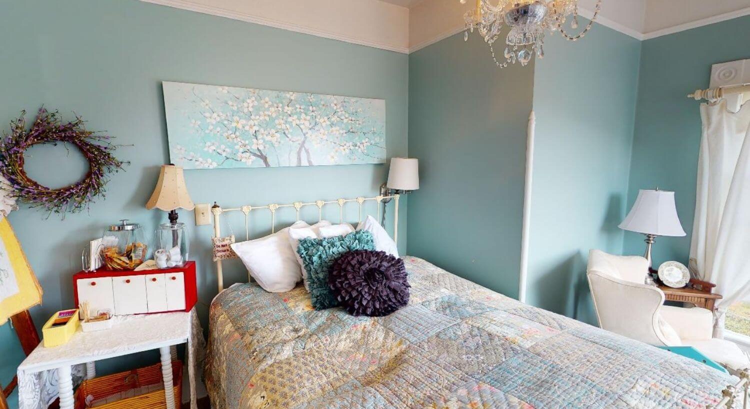 	Bed with pastel colored quilt, white iron bed frame and blue walls