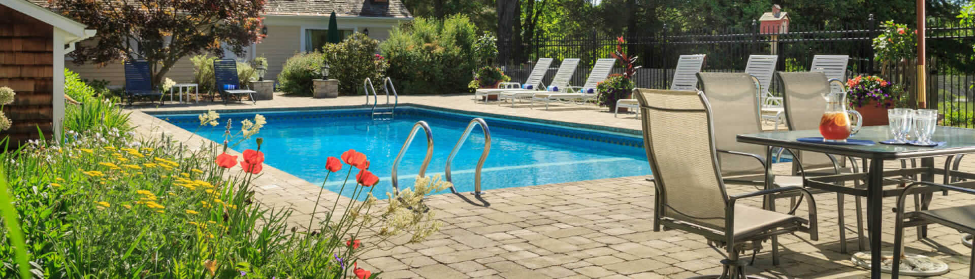Sparkling blue swimming pool with a white brick surround, bordered by flowering plants