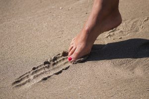 Woman with painted toes drawing line in sand