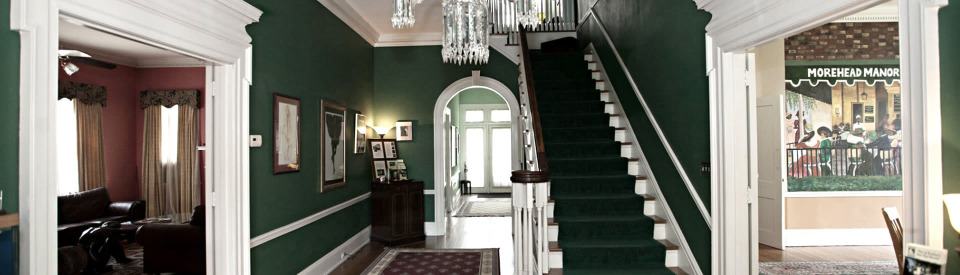 Grand entryway with elegant staircase, decorated in deep green with wood floors and a crystal chandelier