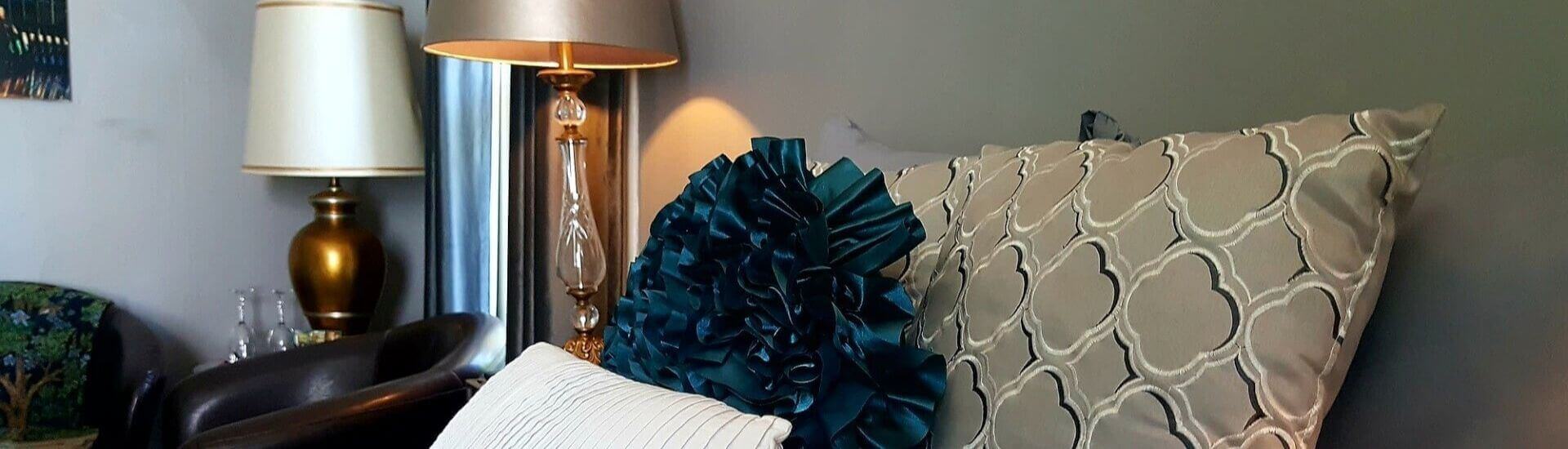 Teal and tan pillows on a bed next to a dark leather club chair and two decorative lamps