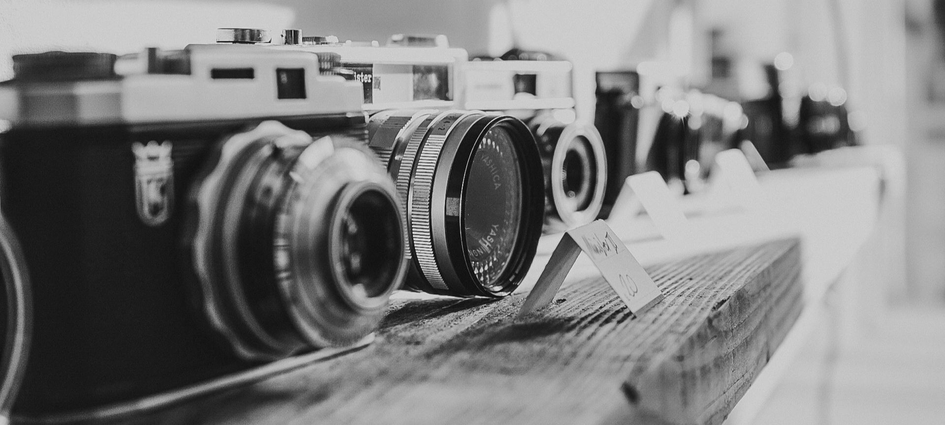 Line of vintage cameras on a wooden shelf in black and white