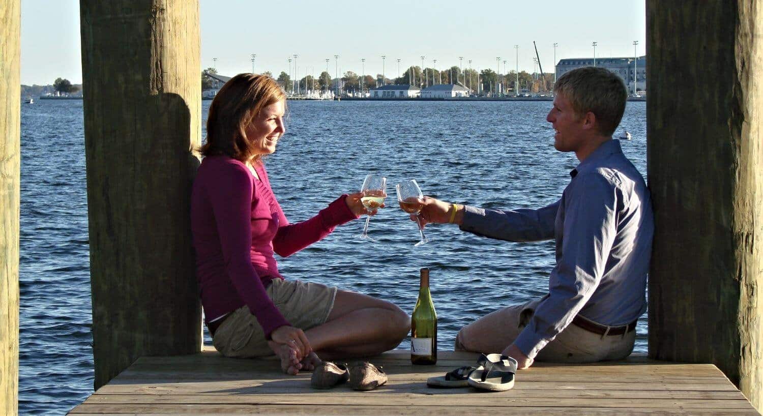 Couple sitting on a dock taosting with wine glasses