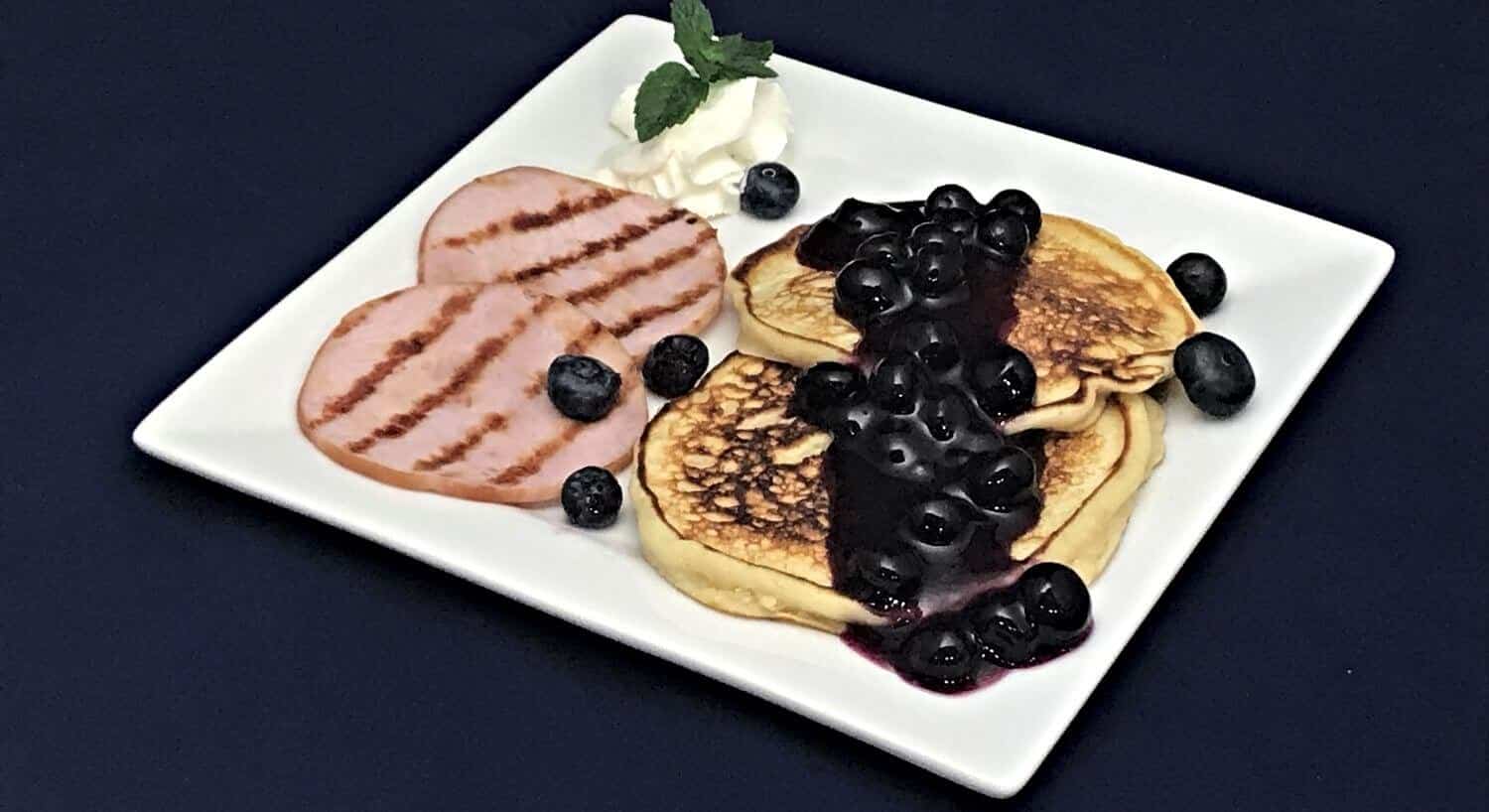 Grilled ham and blueberry pancakes on a white plate