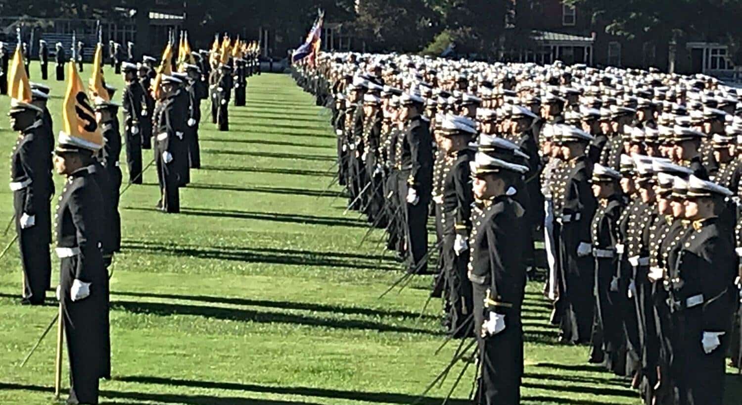 Navy cadets stand at parade rest on a green lawn