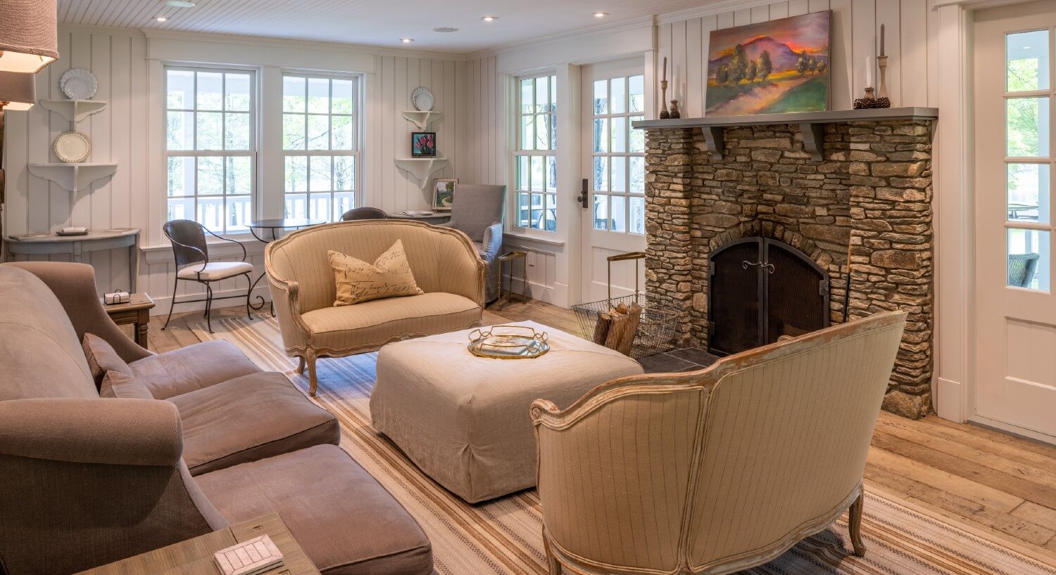 Living room with bright windows, shiplap walls and plush seating in front of a stone fireplace