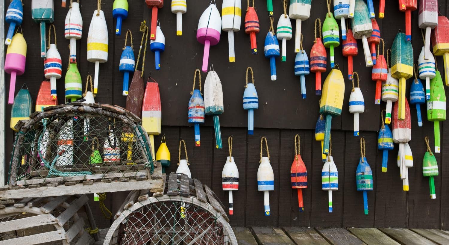 Outdoor wooden wall hanging colorful wooden buoys and a few old lobster traps sitting on the deck