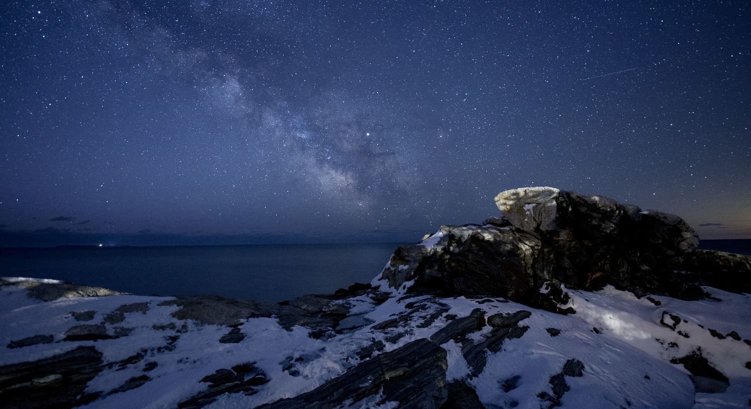 Weathered large rock formations covered by snow near the ocean at night with stars in the sky