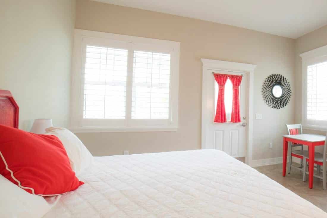 Interior view of bedroom decorated in white with red accents. Open design with windows allowing sunlight in.
