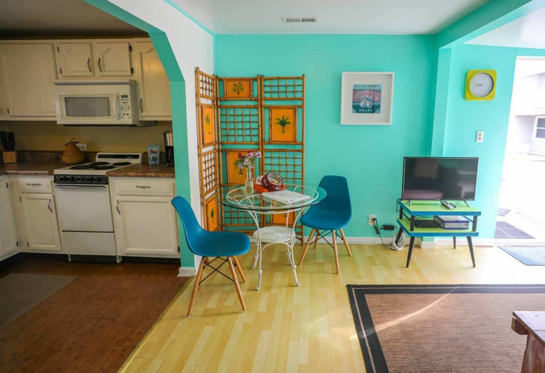 Interior view of sitting area with kitchen visible in background. Blues, oranges, and greens provide colorful contrasts.