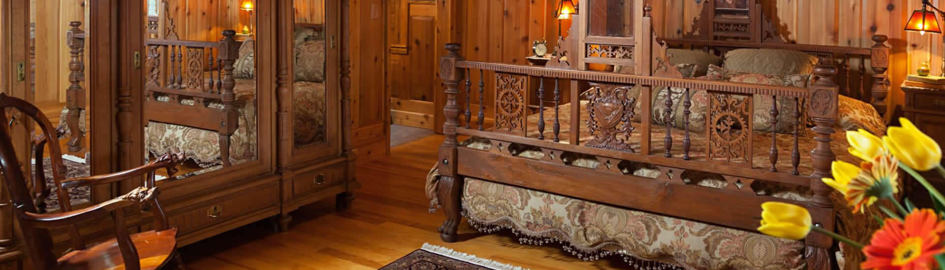 Ornately carved King-sized bed in a wood-paneled room with an enormous wooden armoire and rocking chair