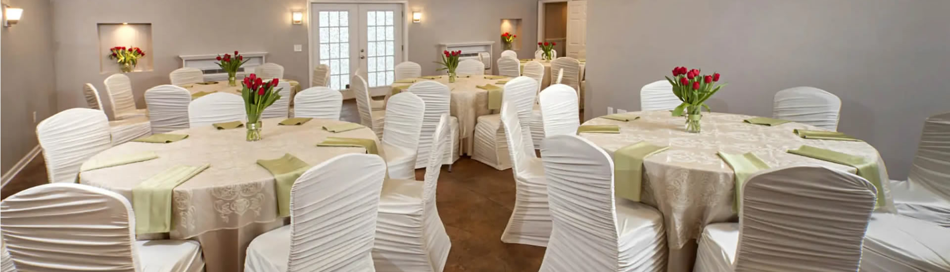 Large meeting room dressed for a wedding with several round tables with green and beige table linens and red tulips
